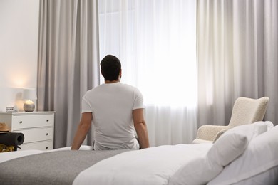 Photo of Traveller sitting on bed in hotel room, back view