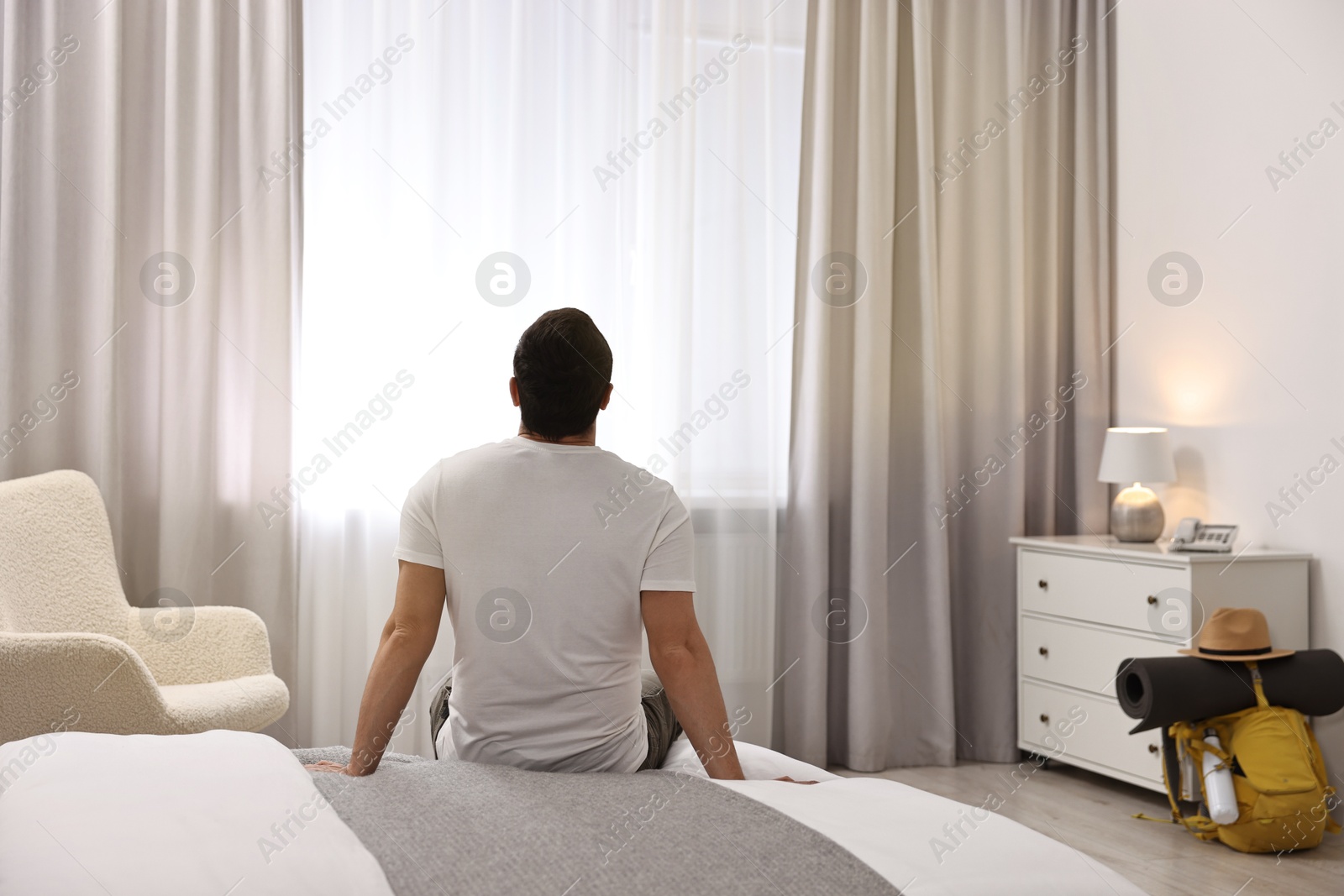 Photo of Traveller sitting on bed in hotel room, back view