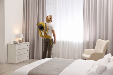 Photo of Traveller with backpack near window in hotel room, space for text