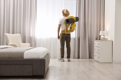 Photo of Traveller with backpack near window in hotel room, back view