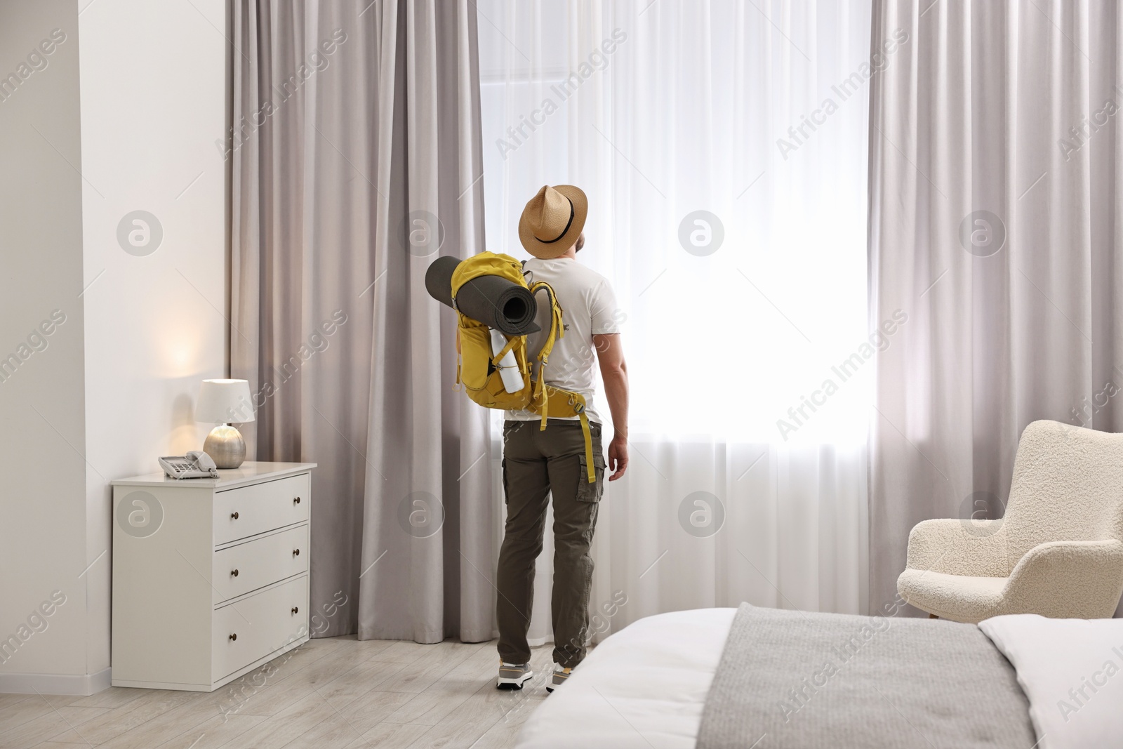 Photo of Traveller with backpack near window in hotel room, back view