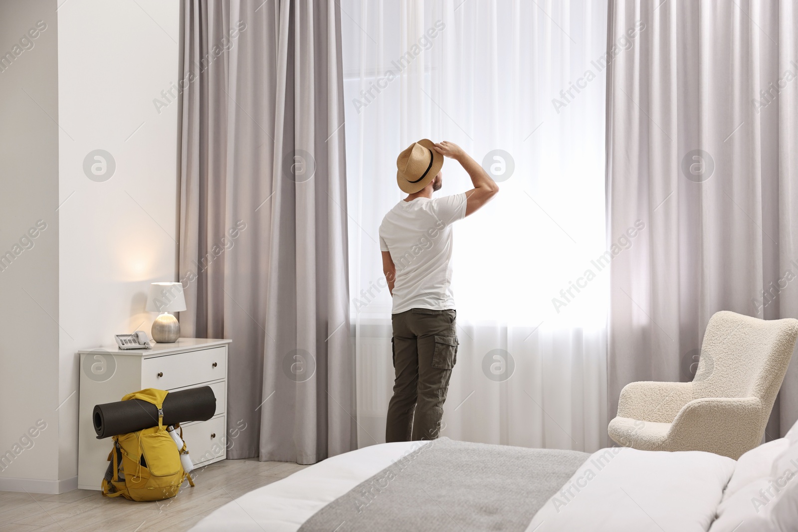 Photo of Traveller with straw hat near window in hotel room