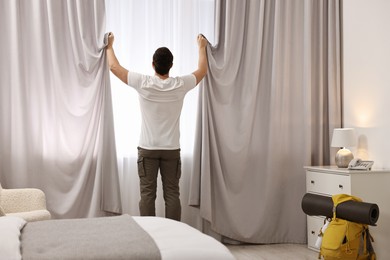 Photo of Traveller opening curtains in hotel room, back view