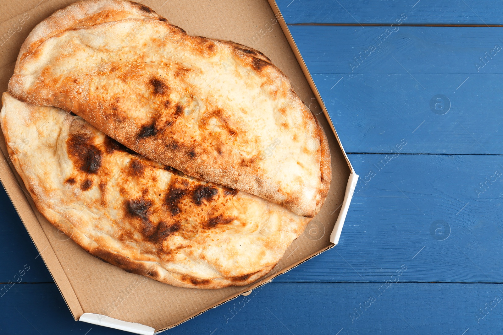 Photo of Tasty calzones in cardboard box on blue wooden table, top view. Space for text