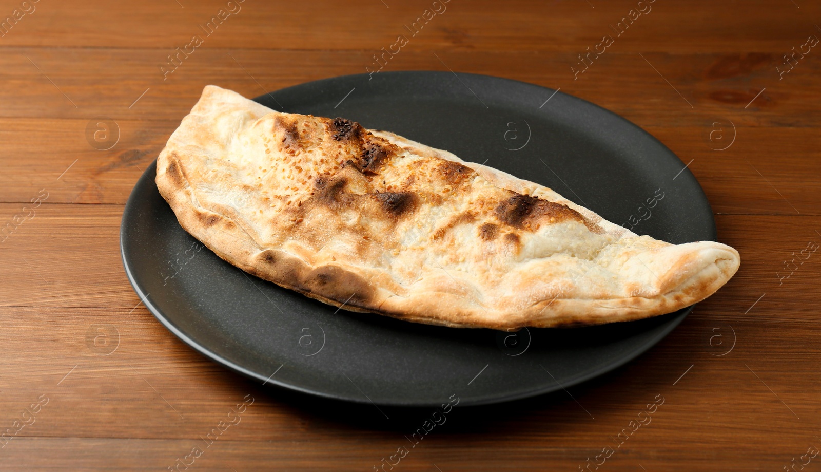 Photo of Plate with tasty calzone on wooden table, closeup