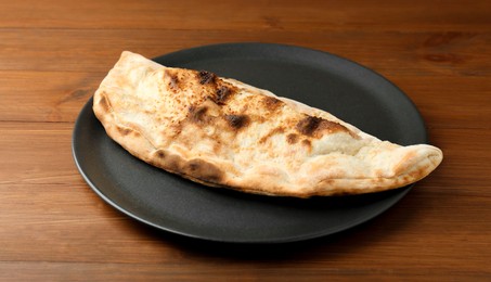 Photo of Plate with tasty calzone on wooden table, closeup