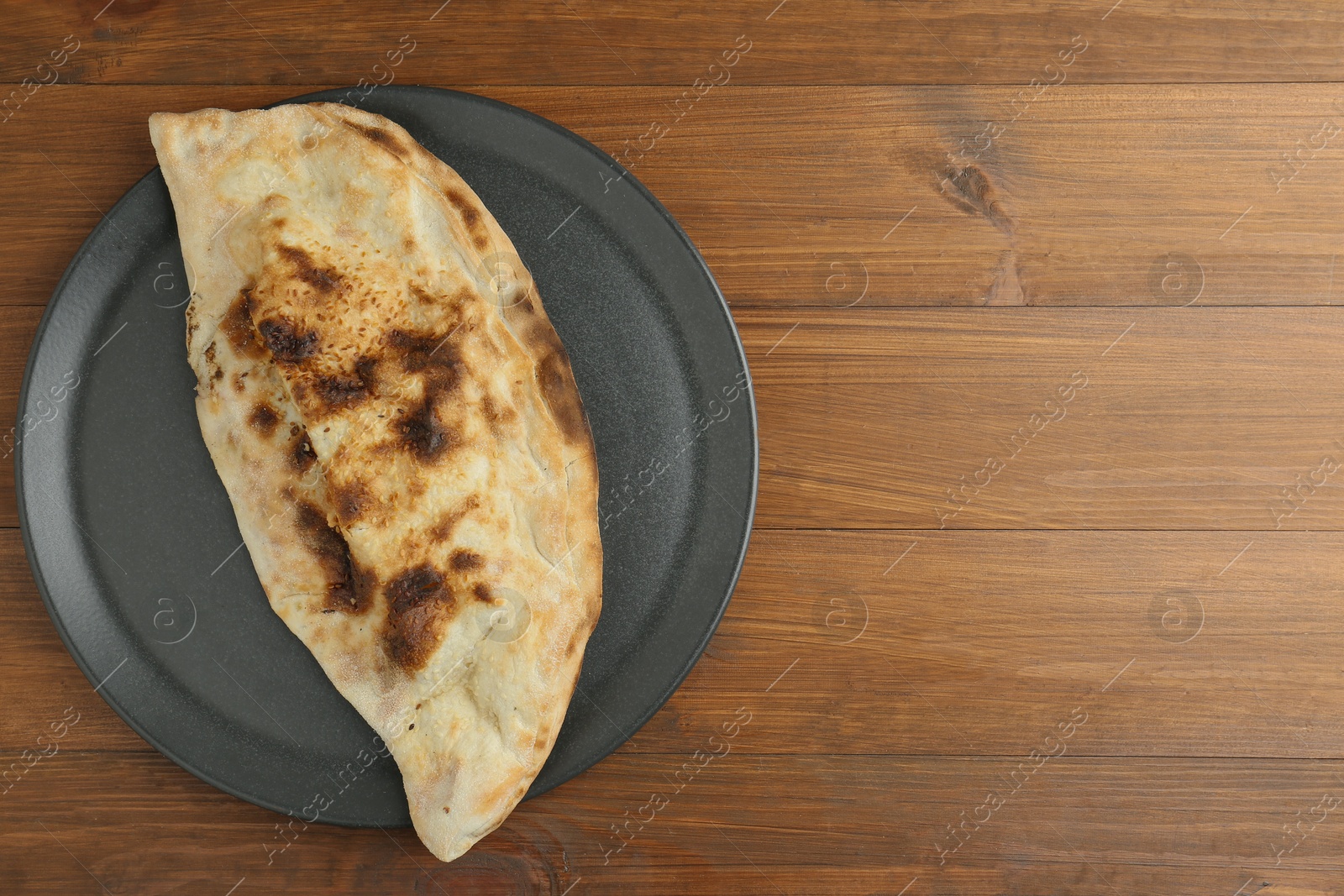 Photo of Plate with tasty calzone on wooden table, top view. Space for text