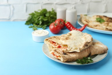 Photo of Halves of tasty calzone with meat, cheese, tomato and sauce on light blue table. Space for text