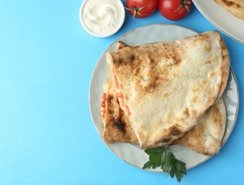 Photo of Halves of tasty calzone, tomato and sauce on light blue table, flat lay. Space for text