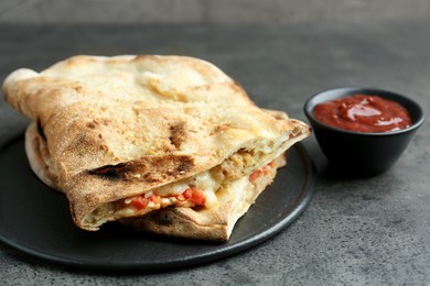 Photo of Halves of tasty calzone with meat, cheese, tomato and sauce on grey textured table, closeup