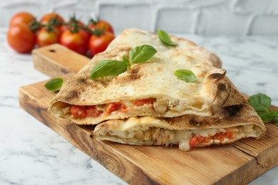 Photo of Halves of tasty calzone with meat, cheese, basil and tomato on white marble table, closeup