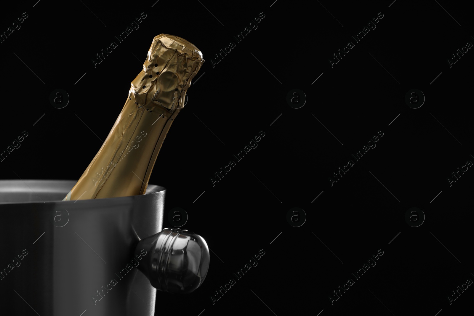 Photo of Bottle of champagne in bucket on black background. Space for text