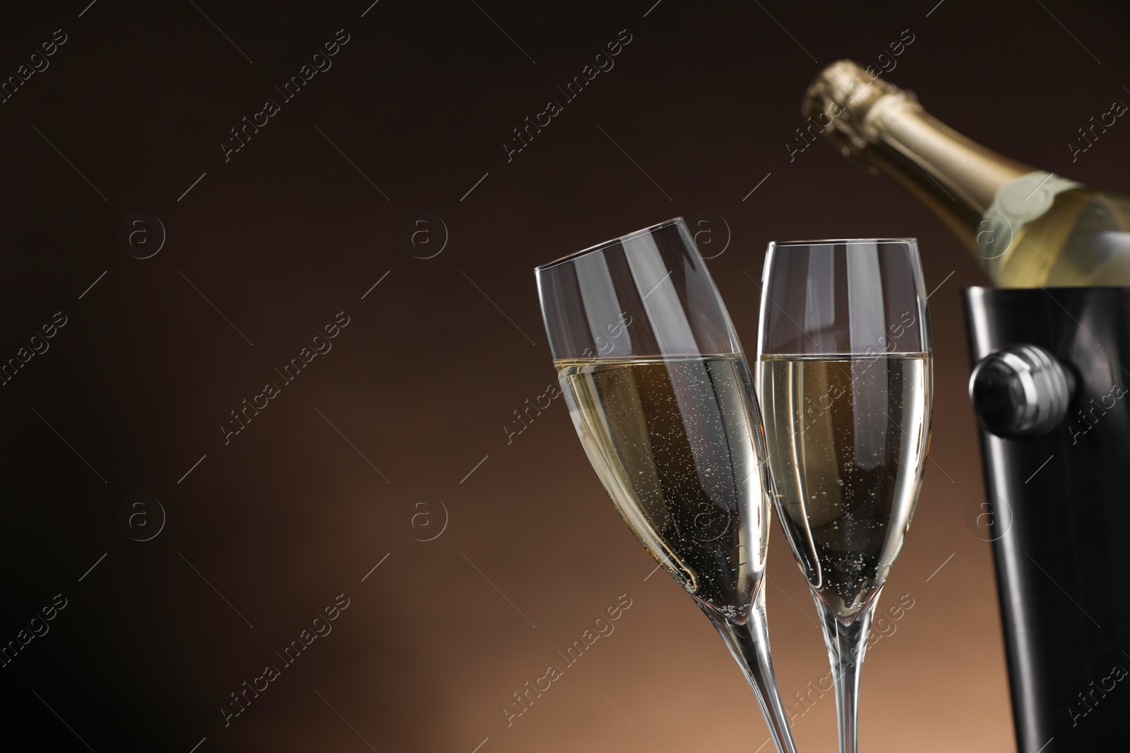 Photo of Champagne in glasses and ice bucket with bottle on brown background, space for text