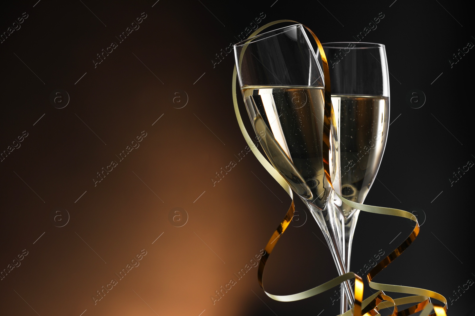 Photo of Champagne in glasses and party streamers on brown background, space for text