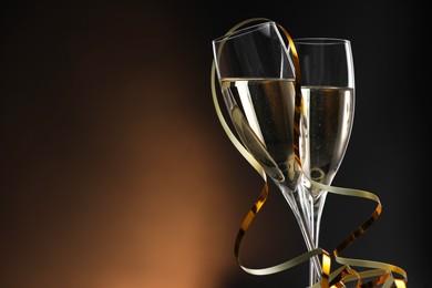 Photo of Champagne in glasses and party streamers on brown background, space for text