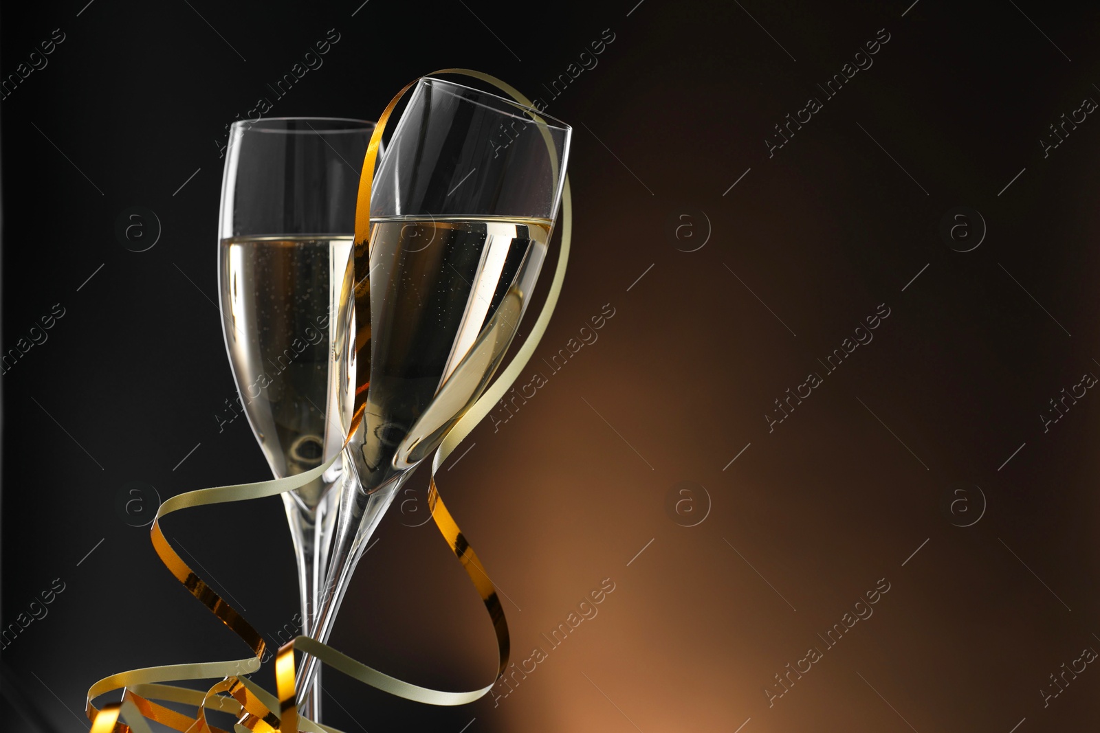 Photo of Champagne in glasses and party streamers on brown background, space for text