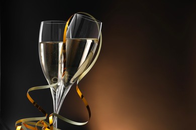 Photo of Champagne in glasses and party streamers on brown background, space for text