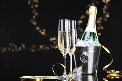 Photo of Champagne and bucket of ice on mirror surface against black background with blurred lights, space for text