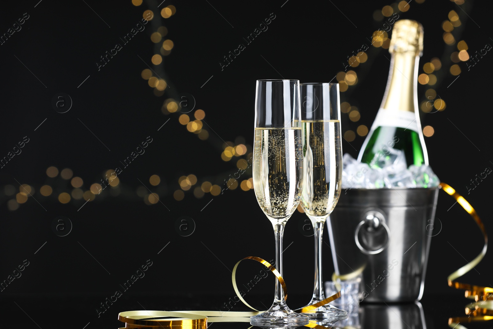 Photo of Champagne and bucket of ice on mirror surface against black background with blurred lights, space for text