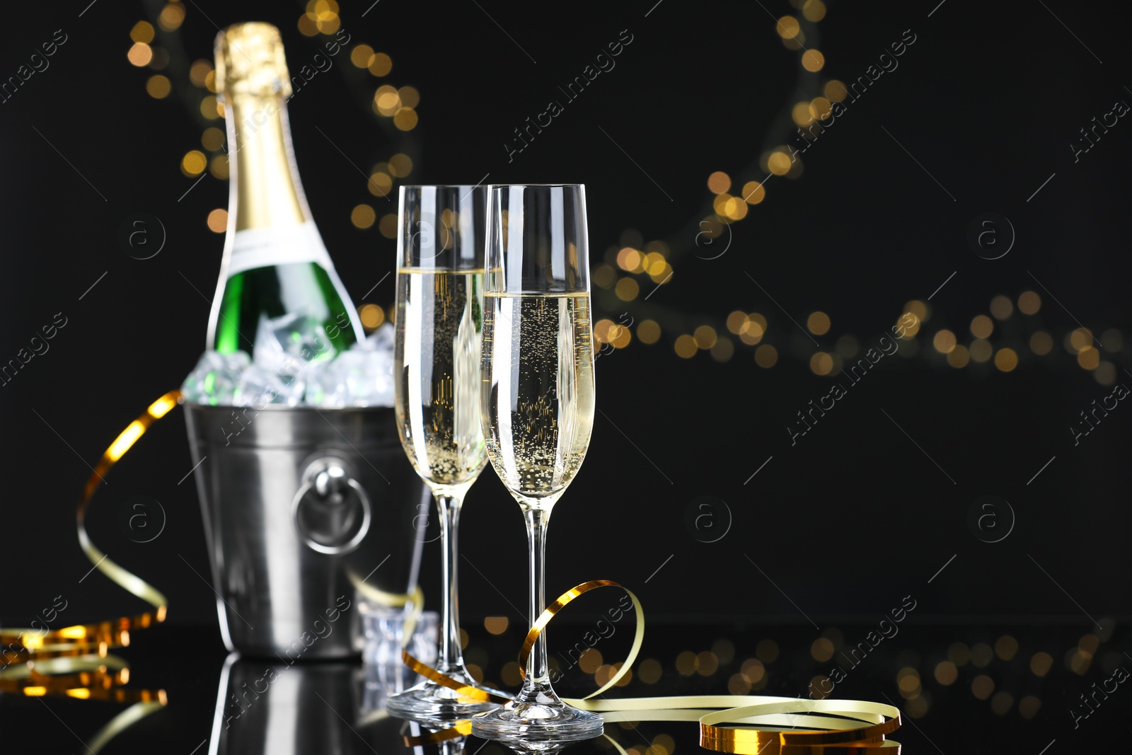 Photo of Champagne and bucket of ice on mirror surface against black background with blurred lights, space for text