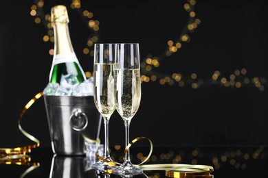 Photo of Champagne and bucket of ice on mirror surface against black background with blurred lights, space for text