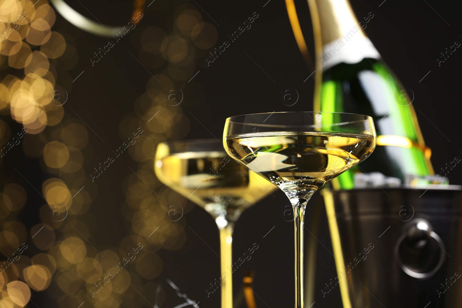 Photo of Champagne in glasses and ice bucket with bottle on dark background with blurred lights, space for text