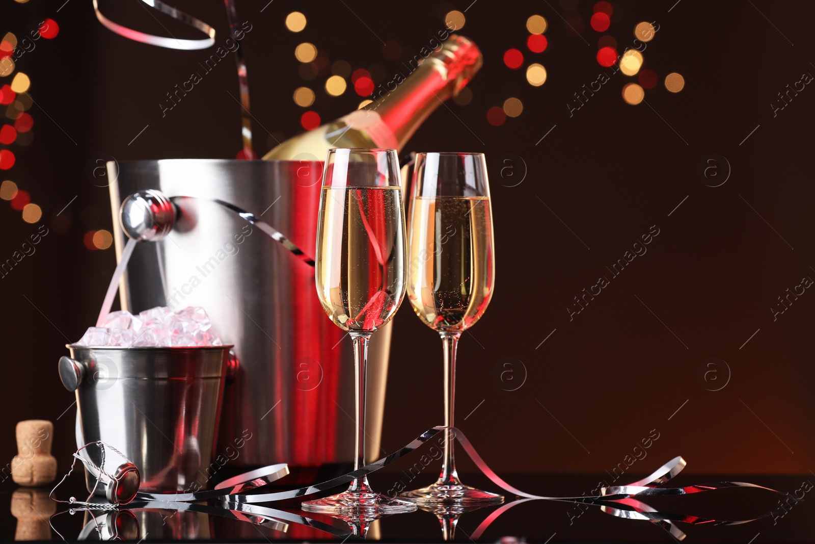 Photo of Champagne in glasses, bottle and ice buckets on mirror surface against color background with blurred lights, space for text