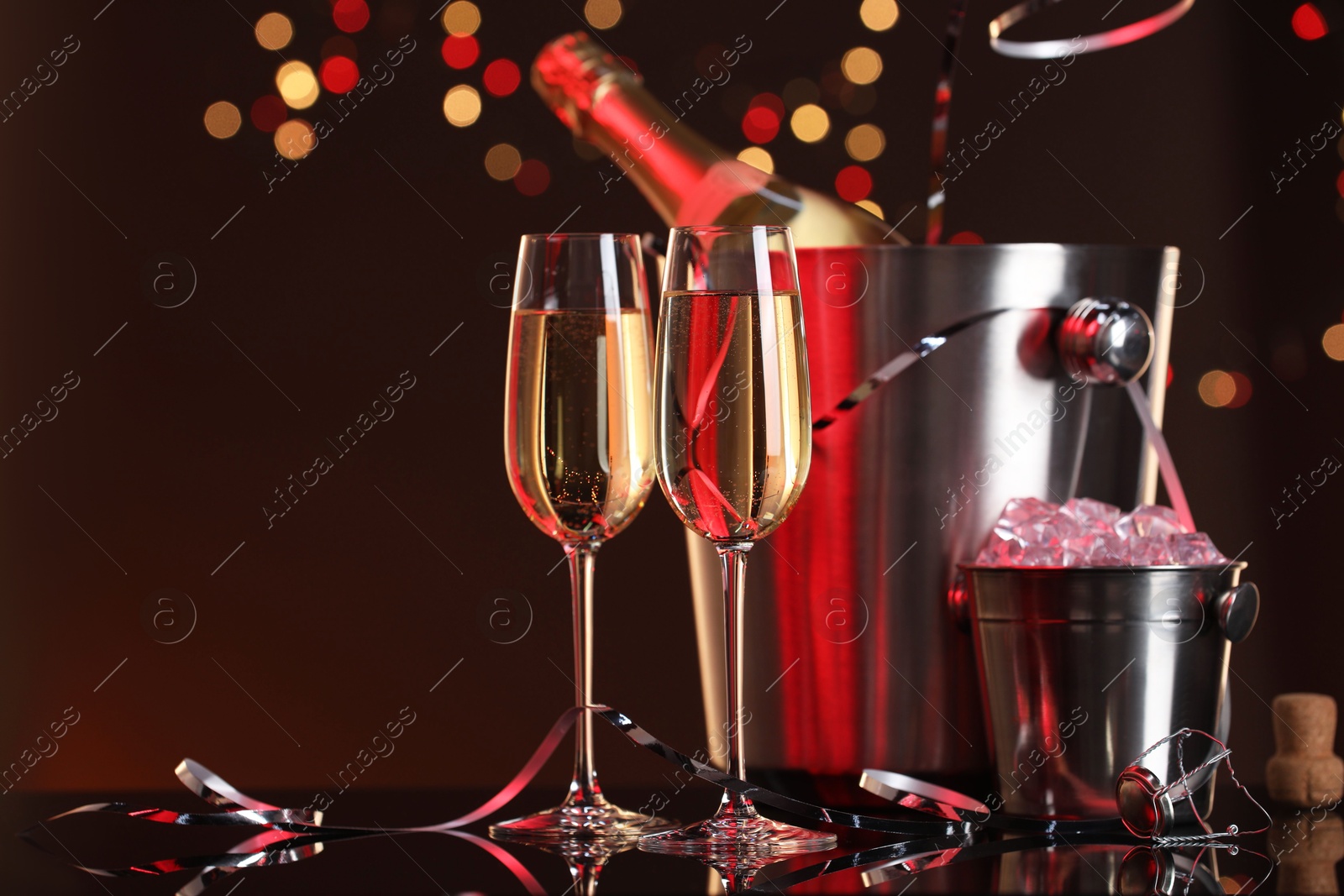 Photo of Champagne in glasses, bottle and ice buckets on mirror surface against color background with blurred lights, space for text