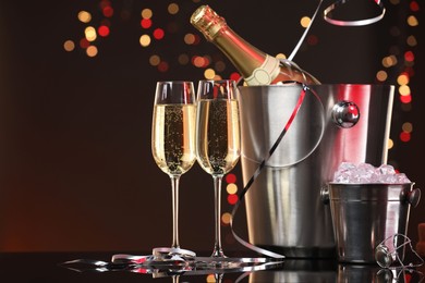 Photo of Champagne in glasses, bottle and ice buckets on mirror surface against color background with blurred lights, space for text