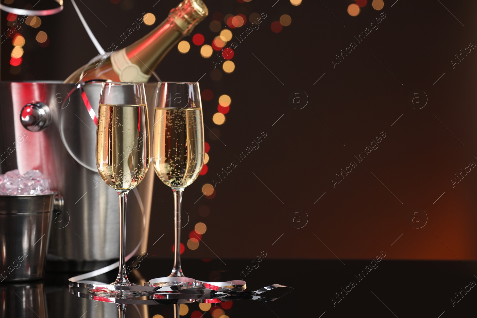 Photo of Champagne in glasses, bottle and ice buckets on mirror surface against color background with blurred lights, space for text