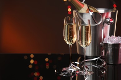 Photo of Champagne in glasses, bottle and ice buckets on mirror surface against color background with blurred lights, space for text