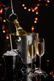 Photo of Champagne in glasses, bottle and ice buckets on mirror surface against black background with blurred lights