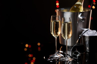 Photo of Champagne in glasses, bottle and ice buckets on mirror surface against black background with blurred lights, space for text