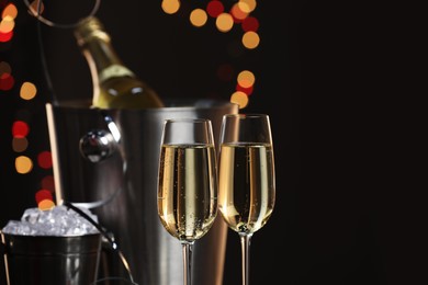 Photo of Champagne in glasses, bottle and ice buckets on black background with blurred lights, space for text