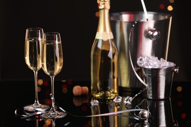 Photo of Champagne in glasses, bottle and ice buckets on mirror surface against black background with blurred lights