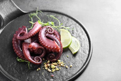 Photo of Tasty boiled octopus tentacles, microgreens, nuts and lime on grey table, closeup