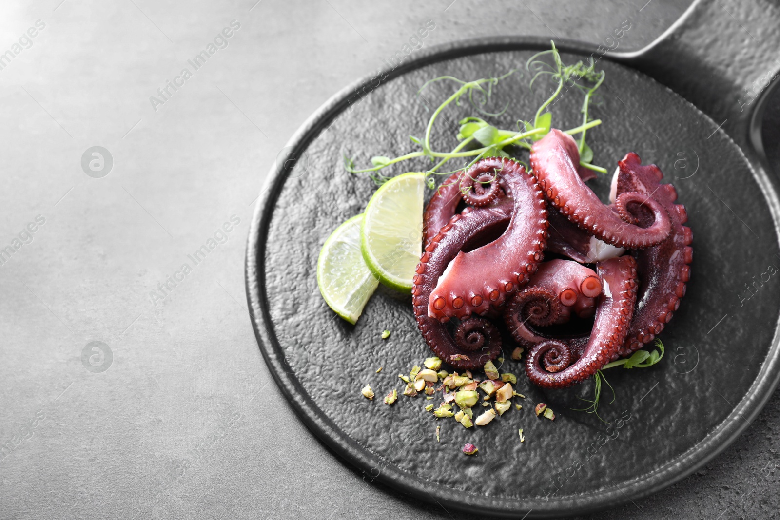 Photo of Tasty boiled octopus tentacles, microgreens, nuts and lime on grey table, closeup. Space for text