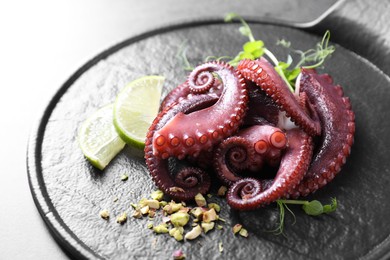 Photo of Tasty boiled octopus tentacles, microgreens, nuts and lime on grey table, closeup