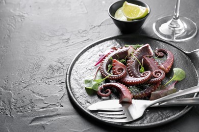 Photo of Tasty boiled octopus tentacles, microgreens and cutlery on grey textured table, closeup. Space for text