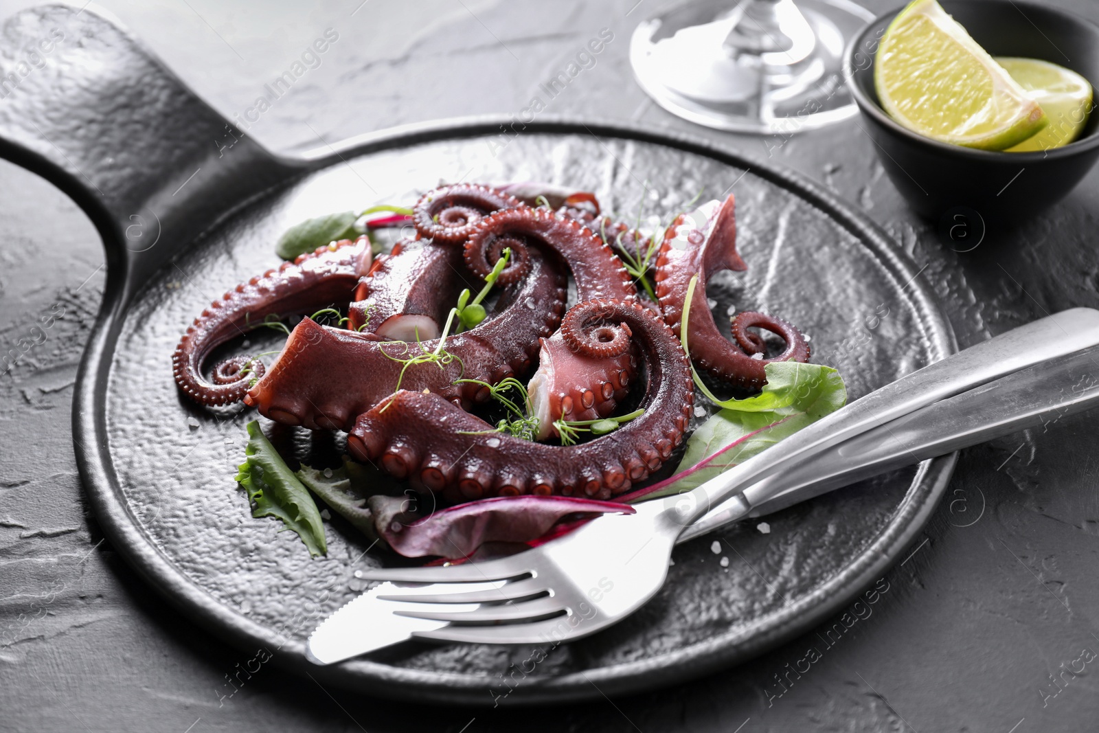 Photo of Tasty boiled octopus tentacles, microgreens and cutlery on grey textured table, closeup