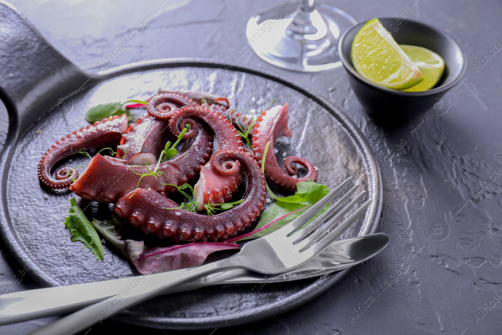 Photo of Tasty boiled octopus tentacles, microgreens and cutlery on grey textured table, closeup