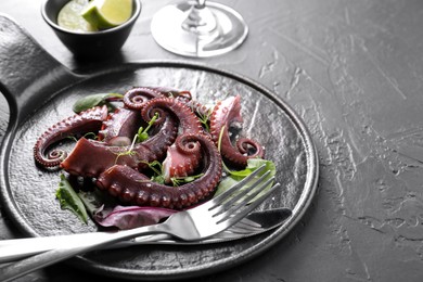 Photo of Tasty boiled octopus tentacles, microgreens and cutlery on grey textured table, closeup