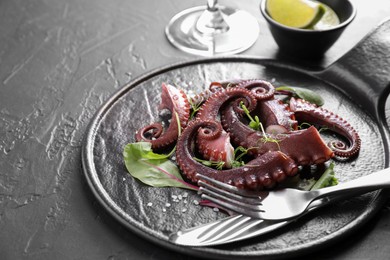 Photo of Tasty boiled octopus tentacles, microgreens and cutlery on grey textured table, closeup