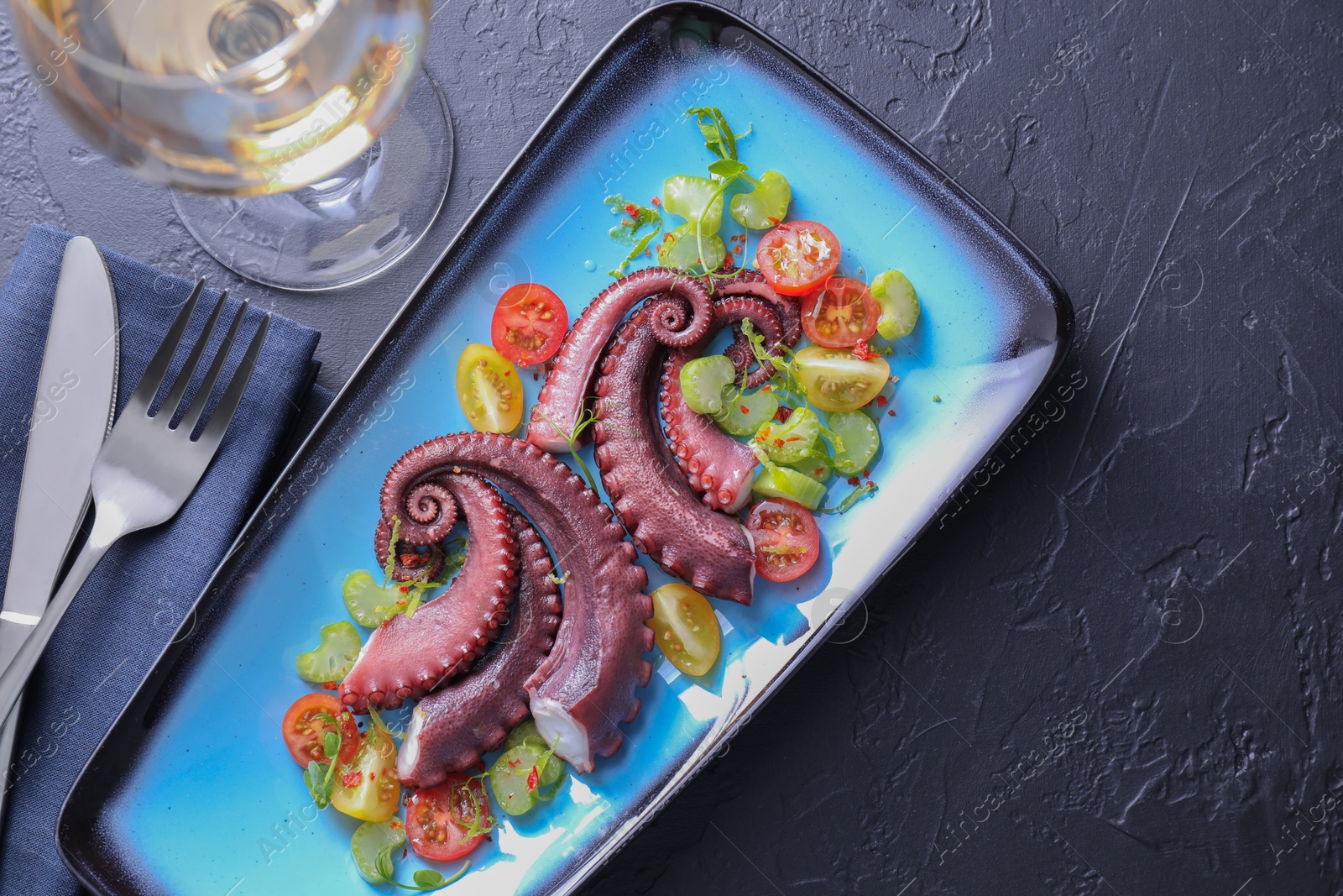 Photo of Tasty boiled octopus tentacles and salad served on grey textured table, flat lay