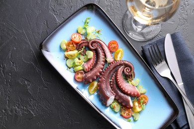 Photo of Tasty boiled octopus tentacles and salad served on grey textured table, flat lay