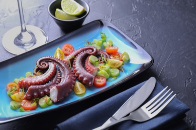 Photo of Tasty boiled octopus tentacles, salad served on grey textured table, closeup