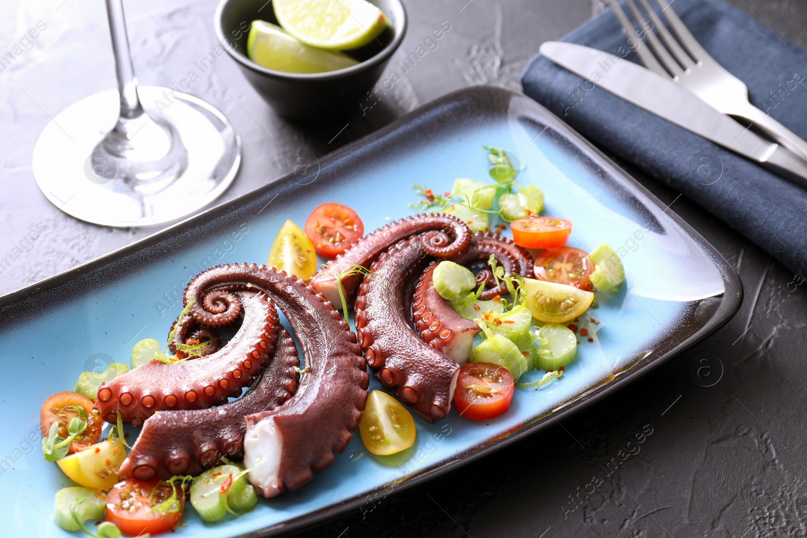 Photo of Tasty boiled octopus tentacles, salad served on grey textured table, closeup