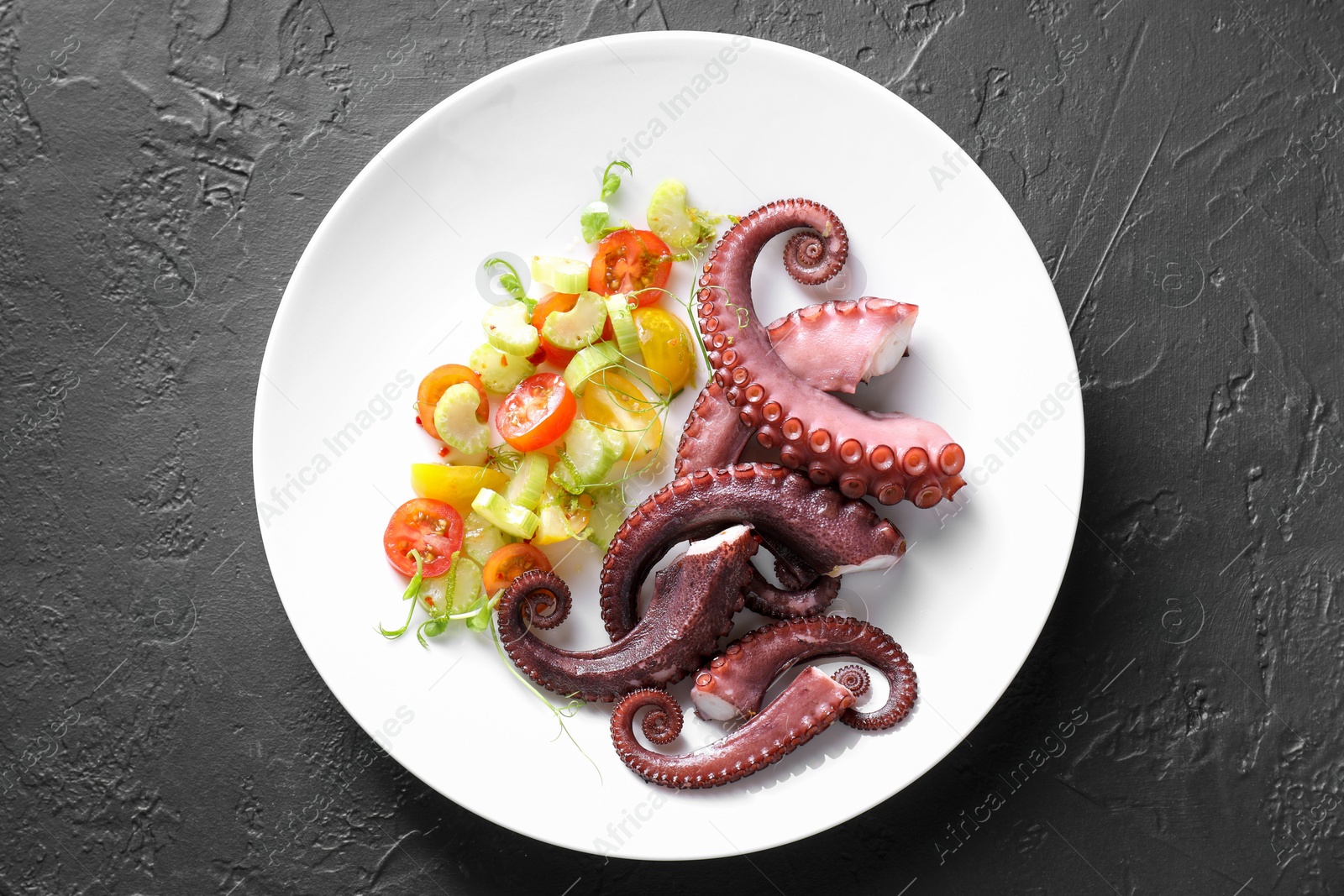 Photo of Plate with tasty boiled octopus tentacles and salad on grey textured table, top view