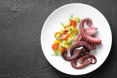 Photo of Plate with tasty boiled octopus tentacles and salad on grey textured table, top view. Space for text