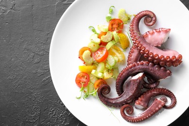 Photo of Plate with tasty boiled octopus tentacles and salad on grey textured table, top view. Space for text